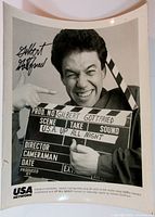 Full view of black and white photo showing Gilbert Gottfried holding a clapperboard labeled USA's Up All Night.