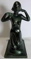 Green painted cast metal sculpture of a kneeling nude female figure shown from front.