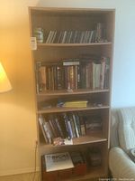Front view of a wooden bookcase filled with books, CDs, and other items.