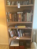 Books, CDs, DVDs on wooden bookshelf, including assorted book titles and media discs