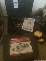 Wide shot of lot showing Bosch drill in case with instruction manual, Husky socket set in black case, and yellow ear protection earmuffs.