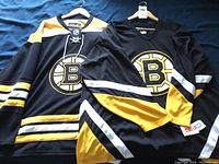 Two Boston Bruins jerseys laid flat on navy blue background, showing front with team logo and design details
