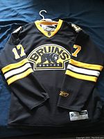 Full view of front black Boston Bruins hockey jersey with yellow and white stripes.