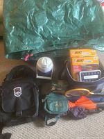 Photo showing green tarp, two packs of BIC disposable lighters, white electric pump, black backpacks, green Aliz cooler bag, and folded umbrellas.