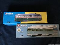 Two Corgi Classics die cast tram models in their original boxes placed side by side, one with bright blue and yellow visuals, the other with detailed tram image on box.