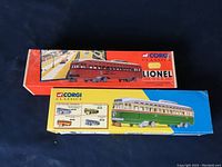 Two boxed Corgi Classics diecast collectible streetcar models: a red and orange Lionel streetcar and a green and cream Philadelphia P.C.C. 55001 streetcar.