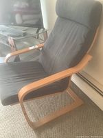 Side angle view of the IKEA Poäng chair showing the bentwood frame and dark fabric cushion, highlighting armrest and cushioning.