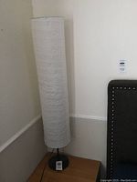 Full view of one white paper shade IKEA floor lamp standing on a wooden surface.