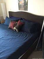 King size bed with padded fabric headboard with metal nailhead trim and dark blue bedding including pillows