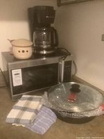 Photo showing Hamilton Beach microwave with digital control panel, Toastmaster coffee maker on top, covered fry pans, and kitchen towels on countertop