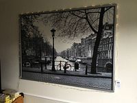 Framed black and white print of urban canal scene with string lights around the frame.