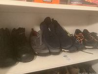 Shelf view of six pairs of men's shoes including black hiking boots, slip-on sneakers, and black and orange ASICS running shoes