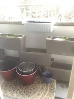Full view of stacked beige plastic attachable planters, white planter above, red and blue pots below on rug