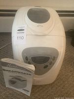 Front view of white Sunbeam bread maker machine with user manual propped in front