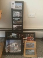 Collection of framed trolley car photographs arranged on floor against wall, showing size comparison and framing styles.