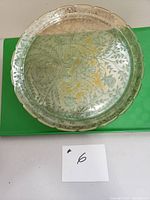 Top view of the Jeannette Floragold iridescent glass platter showing intricate floral and scroll pattern with a scalloped edge on a green background.