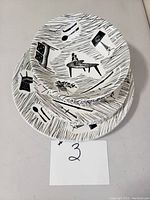 Stacked view of 9-inch plates showing black and white mid-century furniture motifs on ceramic.