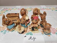 Photo showing all eight Pendilfin bunny figurines arranged together on a floral tablecloth, highlighting the piano and various musical instruments.