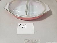 Angled view of pink and white divided casserole with glass lid on, showing both handles and divider in lid.