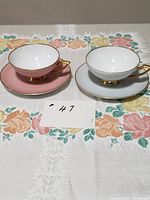 Pair of vintage Heinrich H&C Selb Bavaria Germany teacups and saucers in dusty rose pink and light blue with gold trim shown from front.
