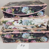 Stacked set of three decorative nesting storage boxes showing floral and script design on lids and sides.