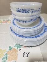 Stacked set showing bowls atop plates with blue floral decorative borders on white milk glass.