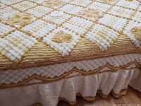 Close-up showing tufted floral and lattice patterns on white and beige cotton chenille fabric, highlighting texture and quality of the bedspread and attached ruffled bed skirt