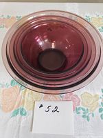 Top-down photo showing all three cranberry glass Pyrex bowls nested inside each other on a floral tablecloth; bowls vary in size and color is consistent deep cranberry.
