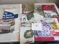 Nine vintage souvenir kitchen and tea towels displayed on a white surface. Towels have assorted sizes and colorful printed designs showing various landmarks and themes such as Cape Breton, Harrods, London, and others.