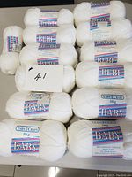 Multiple skeins of white Sayelle Baby yarn stacked, showing labels clearly with 'Baby' and 'Bebe' text, 50g each.