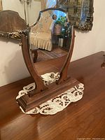 Front angle view showing the shield-shaped mirror with etched floral design, wood side supports, and base.