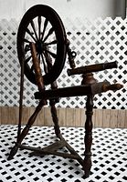 Full view of the antique wood spinning wheel showing the large drive wheel, frame, and treadle.