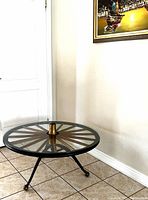 Full view of round glass top coffee table with wagon wheel base, showing three legs with caster wheels and clear glass surface.
