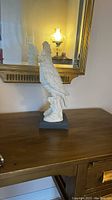Full side view of the white cockatoo parrot sculpture on black base, displayed on a wooden table with mirror behind.