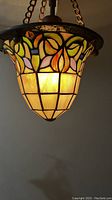 Lit stained glass pendant light showing detailed floral and grid design in stained glass panels.