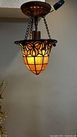 View of stained glass pendant light fixture illuminated from below showing amber toned glass panels with floral geometric design and bronze chain suspension.
