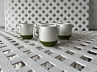 Photo showing four of the six vintage Coleman camping cups grouped together on a white lattice surface, highlighting their size, shape, and two-tone color design.