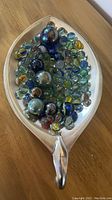 Top view of a silver leaf-shaped dish filled with varied vintage glass marbles.