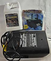 Front view of fog machine, fog fluid container, and box showing product branding and condition