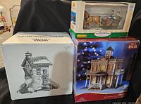 Three boxed items on a table: Lemax horse and carriage in original box, Holiday Time library with some box wear, Dept 56 piece in original box.