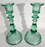 Pair of green glass candlestick holders shown fully in natural light highlighting design and shape.