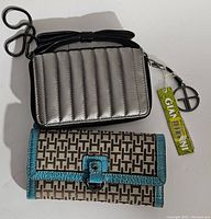 Photo of both wallets, one Tommy Hilfiger with logo pattern and turquoise trim, and one Giani Bernini small metallic silver quilted wallet with attached black strap and tags.