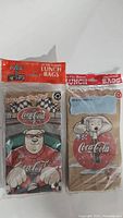 Two sealed packs of Coca Cola lunch bags, one with 20 bags and the other with 15 bags, featuring Coca Cola polar bear artwork and racing theme.
