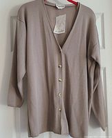 Front view of beige Jessica Scott cardigan hanging on hanger with tags visible.