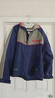 Front and hanging view of the men's vintage Columbia jacket showing blue and gray color blocking, red zipper accents, and fleece lining visible at collar.