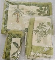 Photo showing folded placemats, napkins and tablecloth in original plastic packaging, all featuring a green and cream palm tree pattern.