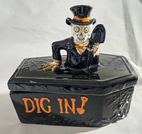 Front and top view of black ceramic candy dish with skeleton figure lid and 'DIG IN!' text on side.