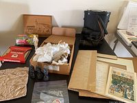 Photo capturing binoculars, wood artwork, boxed chess pieces and pins, documents, and Sterno boxes on a table.