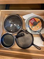 Top view of the lot including a glass lid, Lodge cast iron pan, non-stick pan, and cast iron griddle
