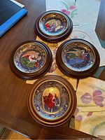 Four wooden framed decorative plates depicting angels surrounded by ornate blue and floral patterns, laid out on a table with boxes visible underneath